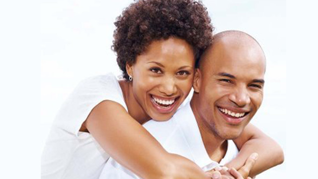 A man and woman are embracing each other with smiles, against a white background.