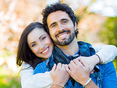 A man and woman embrace each other outdoors during daylight.