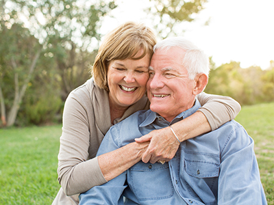 An elderly couple sharing a warm embrace outdoors during sunset.