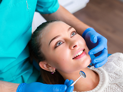 A woman receiving dental care from a dentist, with the dentist holding a dental mirror over her face.